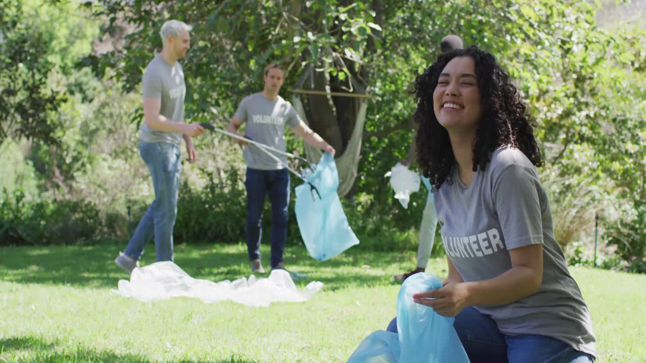 un grupo feliz y diverso de amigos con camisetas de voluntario poniendo residuos plásticos en bolsas de basura al aire libre
