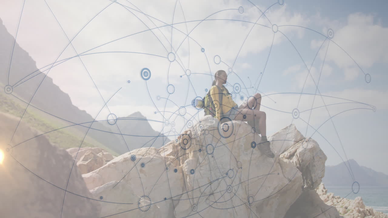 Hiker sitting cross-legged on coastal rock, with technology network overlay displaying data nodes