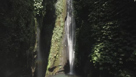 aerial crane shot ascends lush jungle cliff grotto waterfall in bali