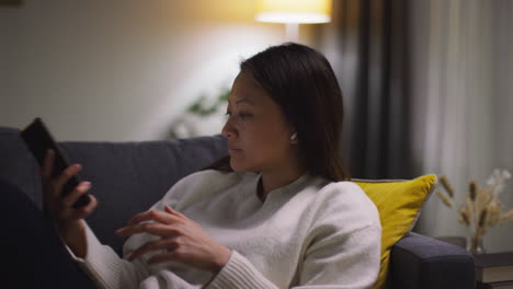 소파에서 집에서 저녁을 보내고 무선 이어을 착용하고 휴대 전화 5에서 음악이나 캐스트를 스트리밍하는 여성의 클로즈업