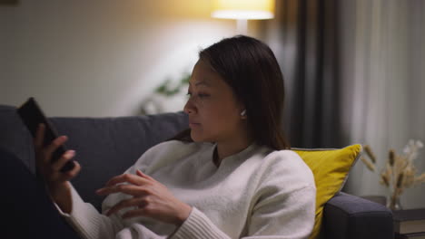 close up of woman spending evening at home on sofa wearing wireless earbuds and streaming music or podcast from mobile phone 5