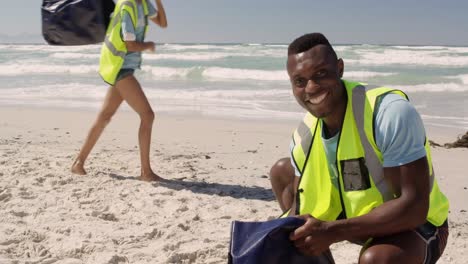 vista frontal de un hombre afroamericano voluntario limpiando la playa en un día soleado 4k