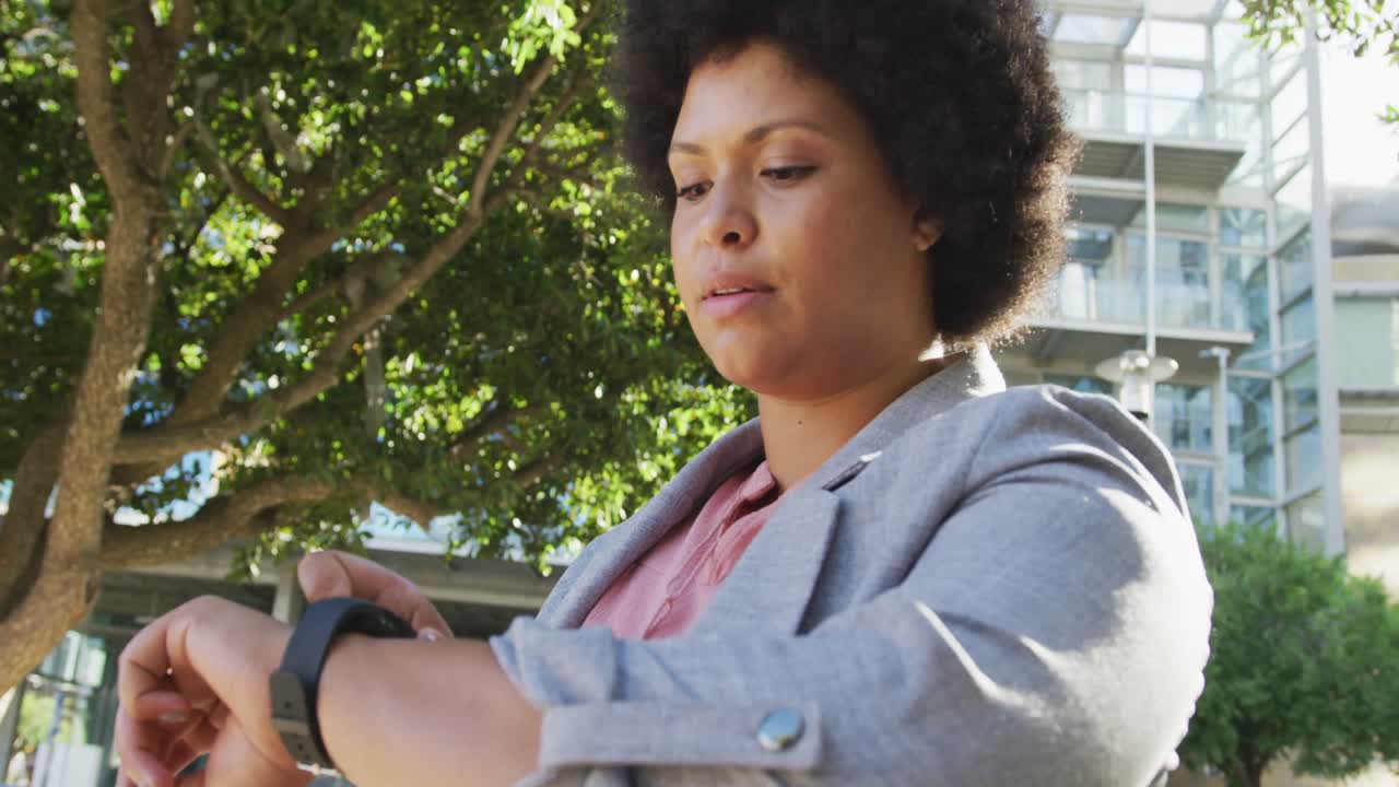 Plus size biracial woman checking smartwatch and walking in city