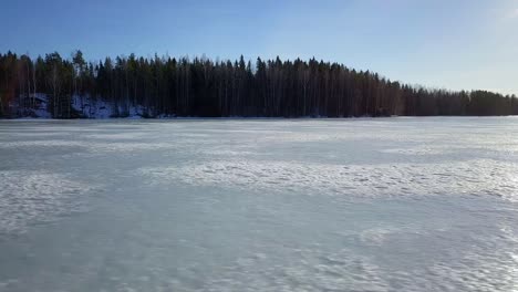 aerial sideways low, sunshine reflected on frozen winter ice lake