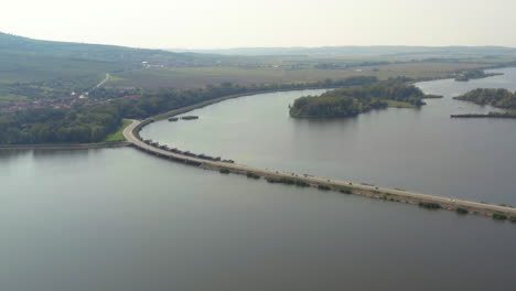 Motorbikes-driving-on-narrow-causeway-in-Věstonice-reservoir,-drone