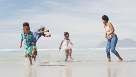 happy african american couple playing with children on sunny beach