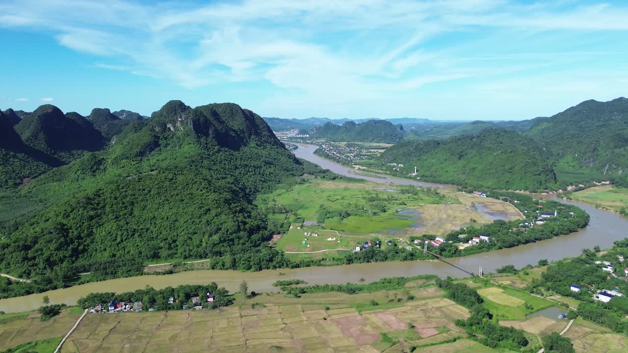 Drone ascends showcasing limestone cliffs, green rice fields and flowing river in Phong Nha