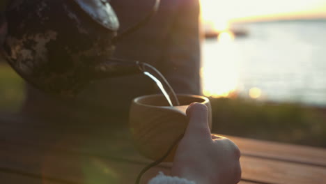 slow motion pouring water from kettle into rustic wooden camping mug