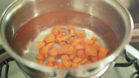 Mano-Femenina-Empobreciendo-Zanahorias-Picadas-En-La-Sartén-Con-Agua-En-Cámara-Lenta