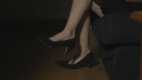 close up of women's legs with black high heels sitting down, crossing her legs and dangling her feet