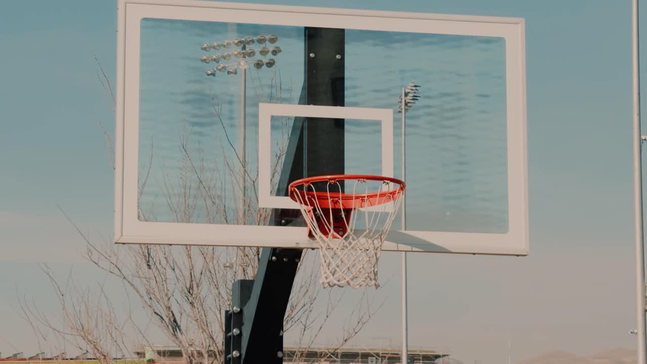 Panoramica lenta e zoom delicato su un canestro da basket vuoto all'aperto con il cielo sereno come sfondo.