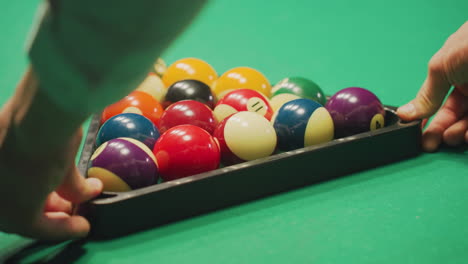 close-up back shot of young hand in white shirt gently rolling a well-arranged set of colorful billiard balls in triangle formation on green pool table