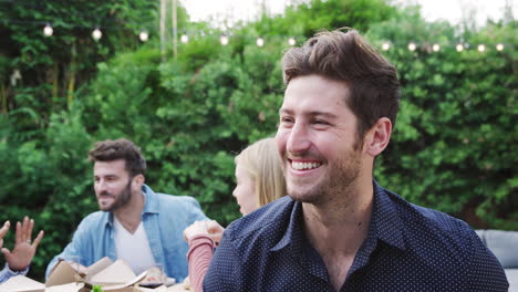 portrait of man with friends at home sitting at table enjoying food at summer garden party