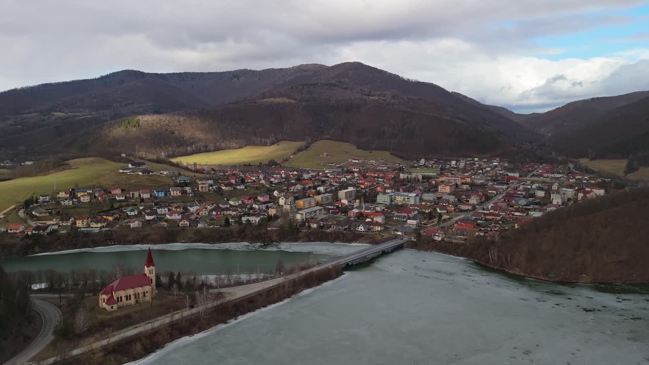 Margecanyn kylässä Itä-Slovakiassa on Kostol sv Margity -katolinen kirkko, jota ympäröivät kukkulat, metsät ja jäätynyt Ružínin tekojärvi pilvisen talvitaivaan alla tässä ilmapanoraamassa.