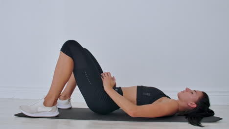 Portrait-of-young-motivated-athletic-female-making-pelvis-lifting-with-weights-indoors