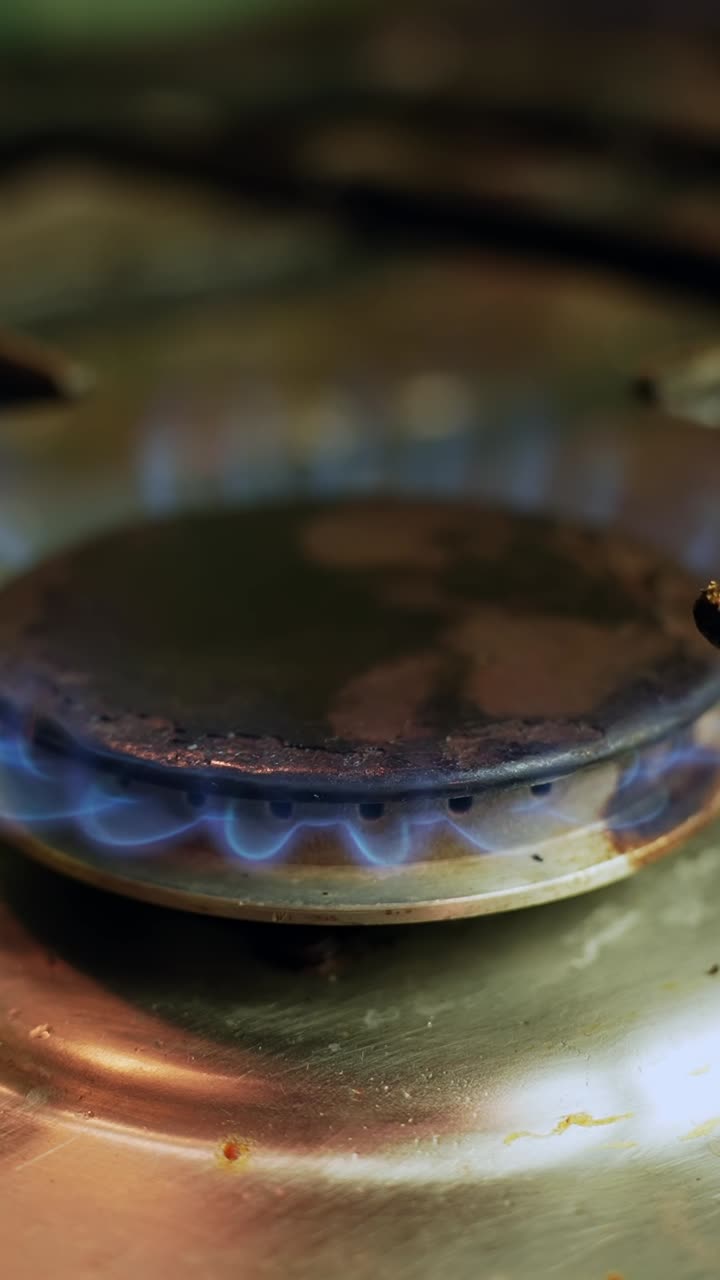 Slow motion close-up of a gas stove burner with steady blue flame on stainless cooktop, showing heat, energy, and cooking power. Vertical macro b-roll