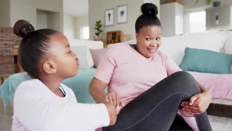 happy unaltered african american mother and daughter doing yoga stretching at home, in slow motion