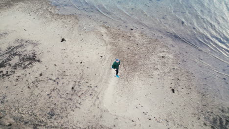 Tracking-top-shot-of-a-runner-on-the-beach-by-the-water-in-winter