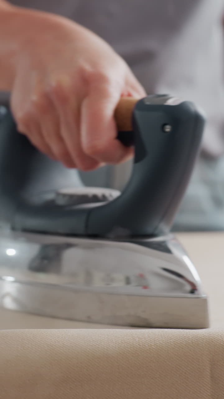 천을 누르는 백인 여성의 타이트한 클로즈업, 스팀과 모션이 있는 스튜디오 배경, 솔기 정렬을 확인하는 재단사, 의복 가장자리를 마무리하는 장인, 기술에 중점을 둔 부티크 생산 분위기