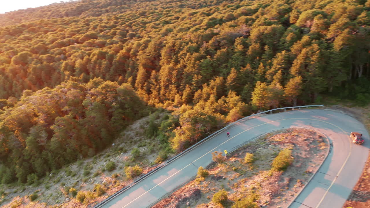 날카로운 머리핀 굽힘, 밝은 햇빛을 돌리는 시골길에서 롱보드 라이더의 공중 전망