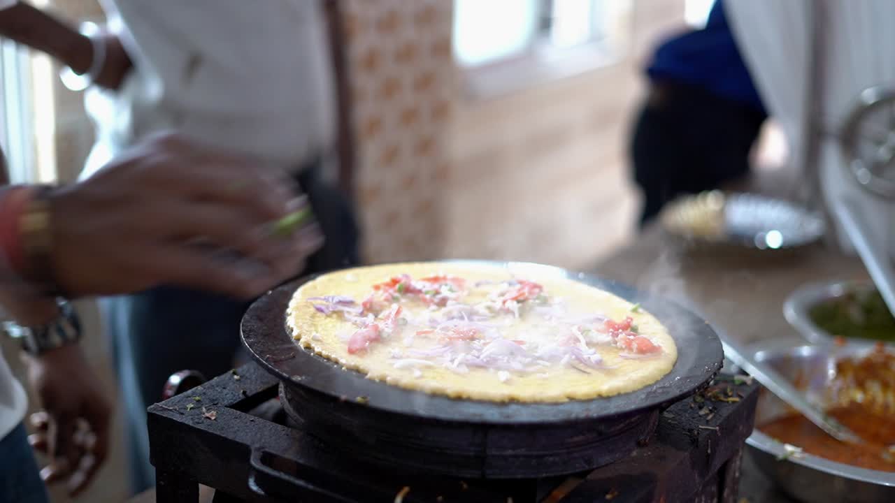 Close up shot of a man sprinkling onions and spices on top of the Dosa while preparation in a shop