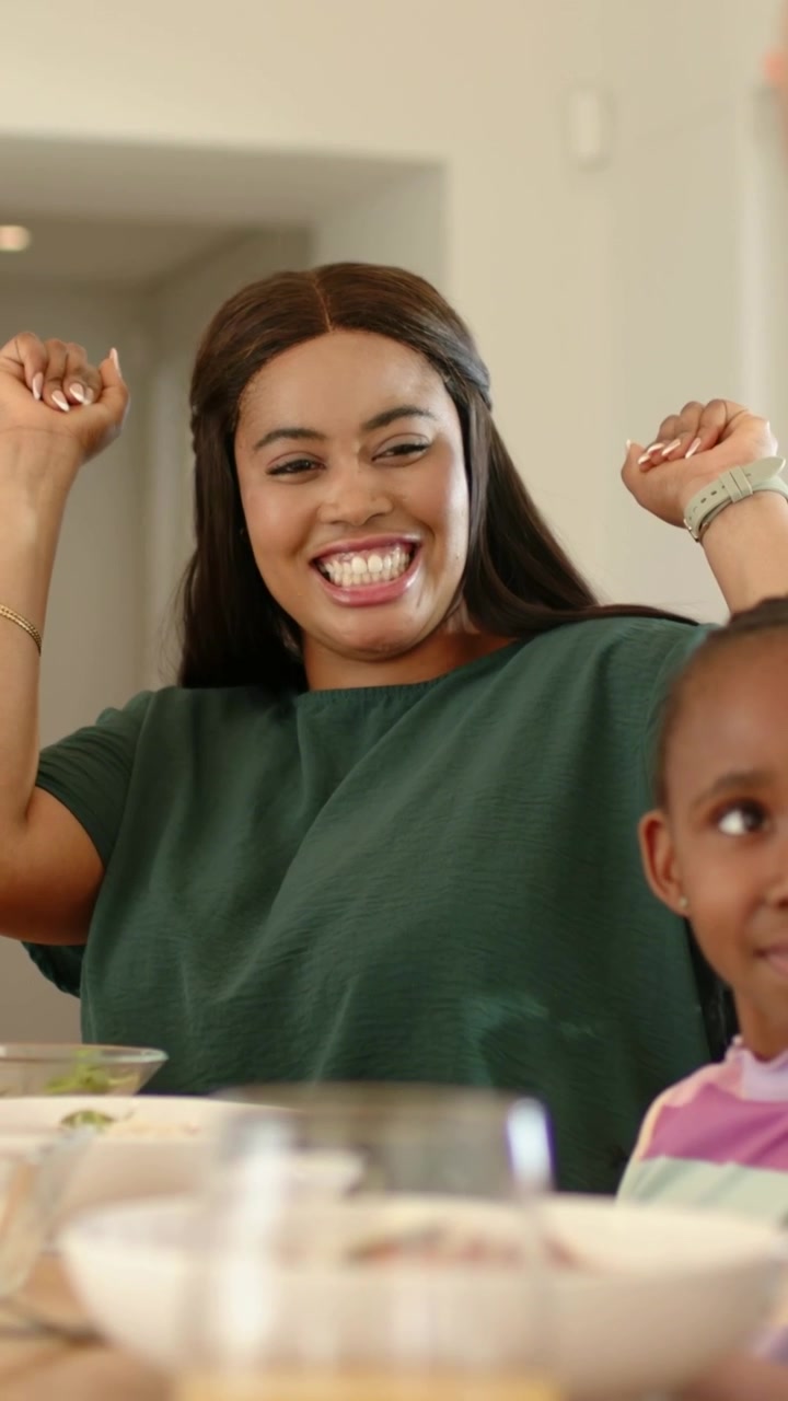 Vertical video: Child reaching up celebrating, mom high-fiving in kitchen in green top with bowls