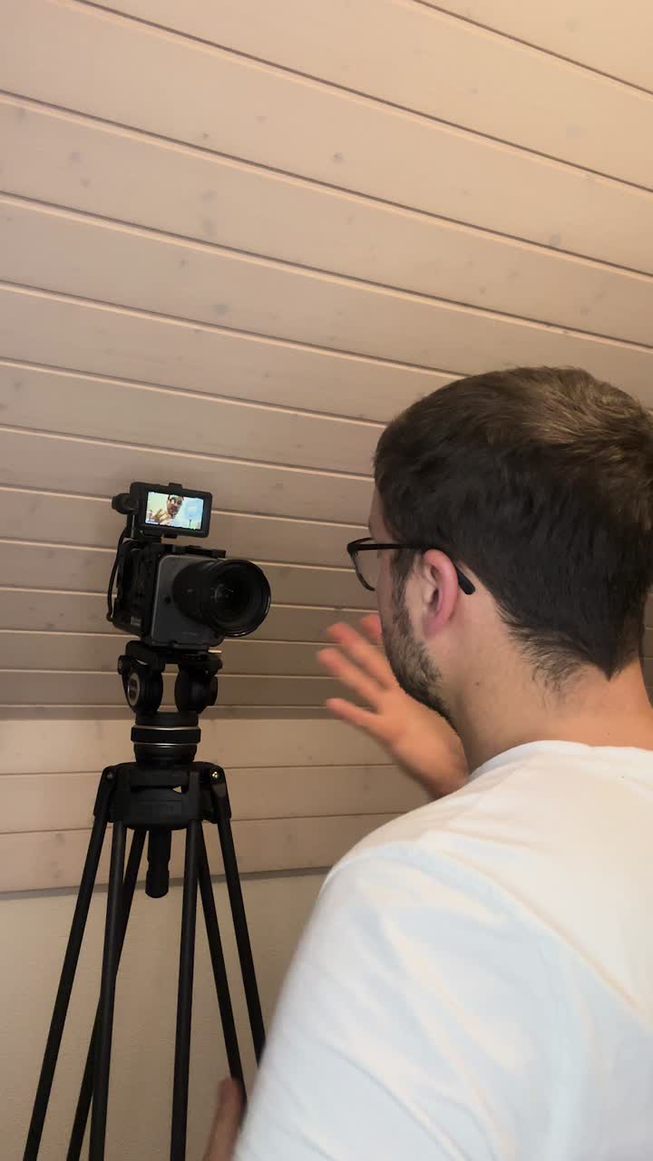 A man adjusts a professional camera on a tripod while checking the framing on the flip screen, preparing for a self-recording or video shoot