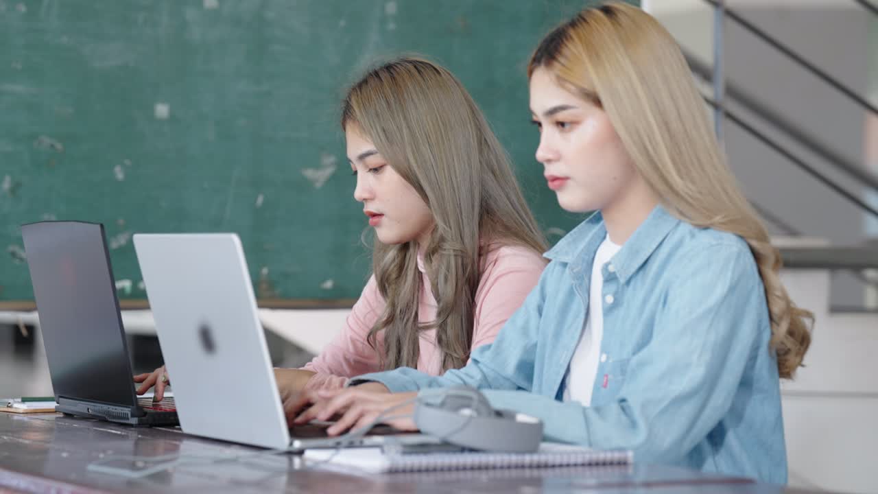 Two Asian girls student partners are working on a laptop help study together