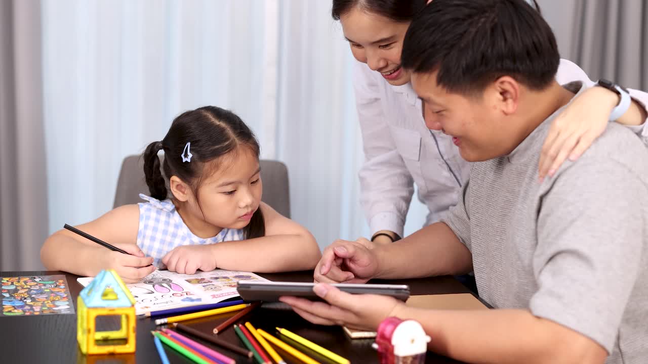 Parents assist young daughter with homework, using tablet and colored pencils in bright home setting