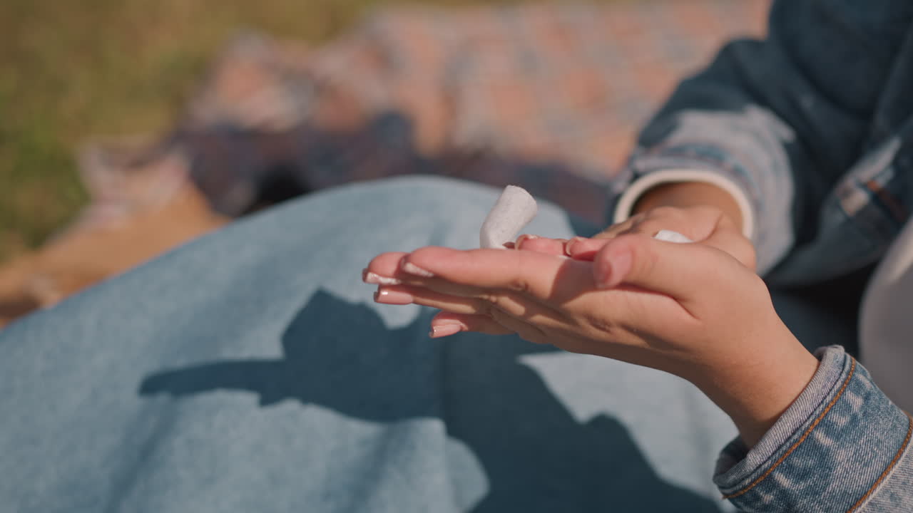 Primer plano de manos secándose con un pañuelo al aire libre, joven con chaqueta vaquera sentada en una manta de picnic secándose suavemente las palmas y los dedos con un pañuelo suave bajo la cálida luz del sol, uñas detalladas, ambiente tranquilo