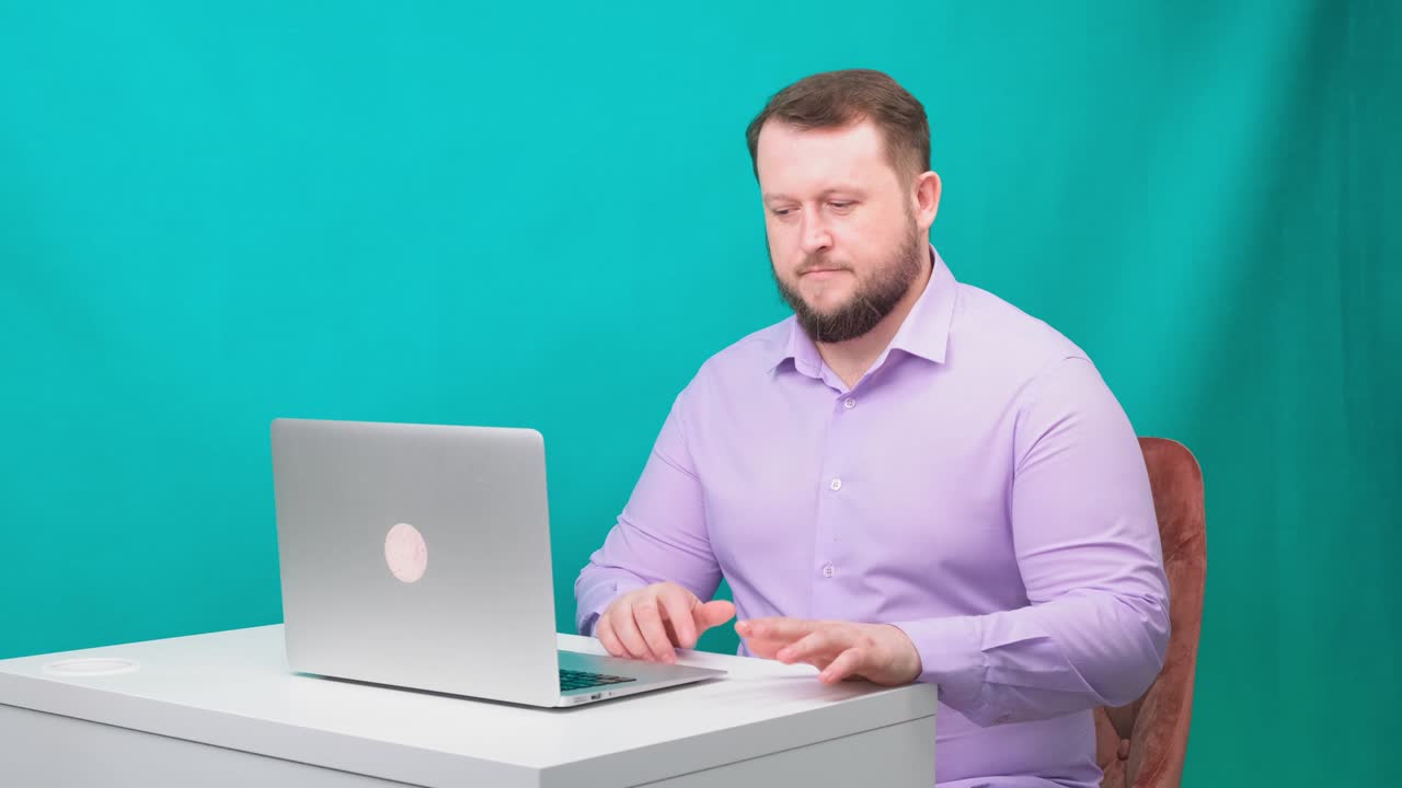Young happy businessman holds a conference meeting at a laptop, a man is nervous and worried, on a green screen. Portrait of a male talking man looking into his laptop. Man working at his desk in the office
