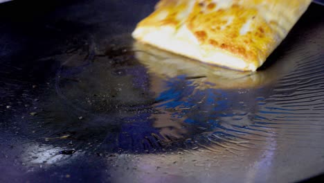 el vendedor de comida callejera está friendo y volteando murtabak, un panqueque de tortilla picante relleno con trozos de verduras y carne picada, en aceite caliente con una espátula y un tenedor