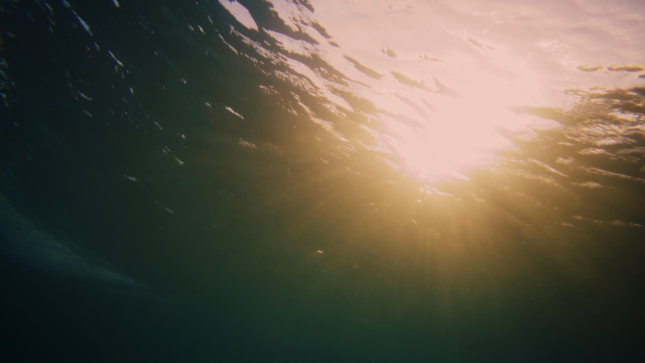una luz dorada naranja brillante brilla a través de las olas subacuáticas que rompen con el surfista.
