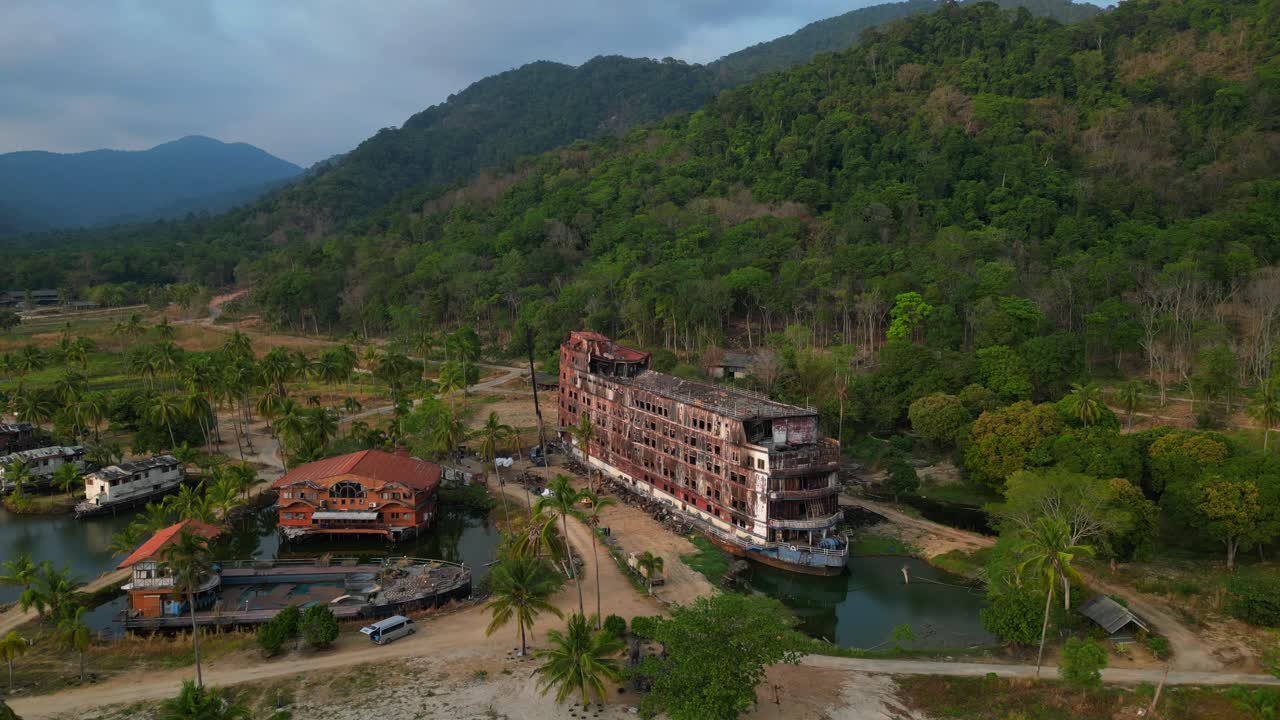 abandoned rusty ghost ship on Koh Chang on tropics island bay, Thailand, during sunset, with a crane working on it. Unique aerial view flight panorama overview drone