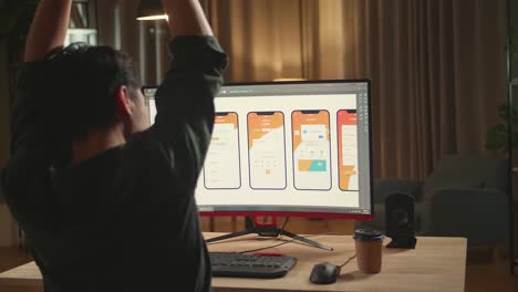 Asian Male Mobile Application Developer Stretching While Works With Graphics On His Personal Computer. He Works At Night