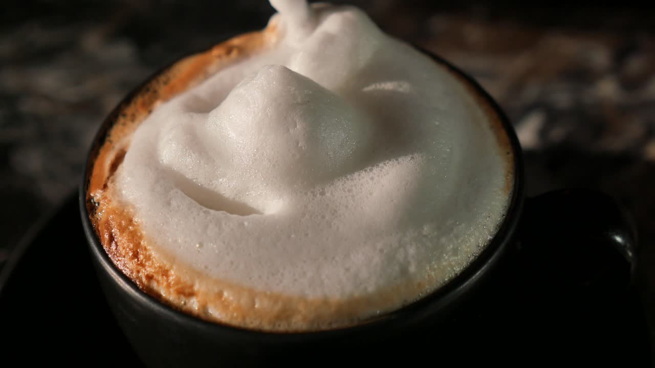 Cucchiaio che mescola delicatamente la schiuma bianca sulla superficie di una bevanda al caffè