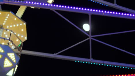 ferris wheel attraction spinning with moon in the background, evening, night, close up