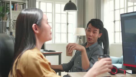 happy asian female video and sound editor works with her male colleague on a project on her personal computer. they work in a creative loft office