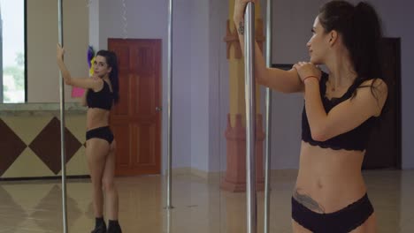 Latina-pole-dancer-admires-her-body-in-the-mirror-while-holding-the-pole-in-a-dance-studio