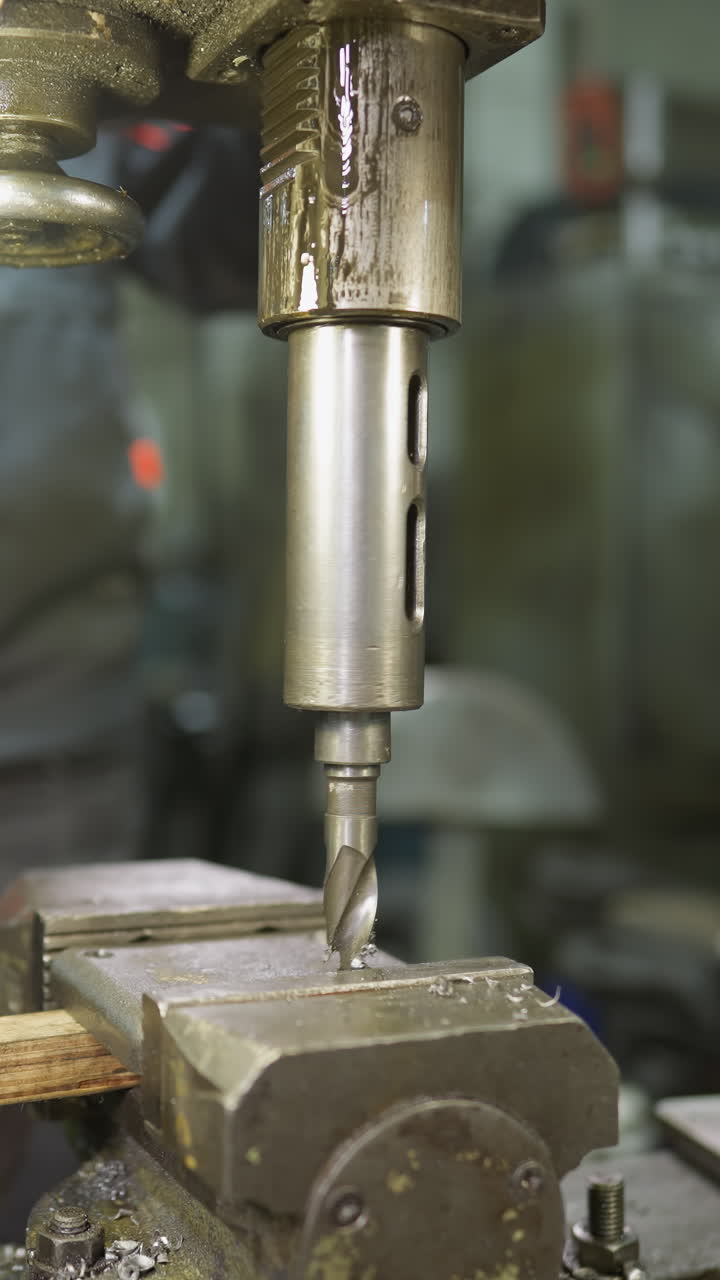 Punta da trapano in movimento su un pezzo di metallo con un operaio d'officina che guida il processo