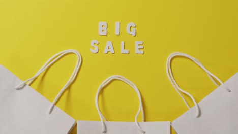 big sale text in white and gift bags with string handles on yellow background