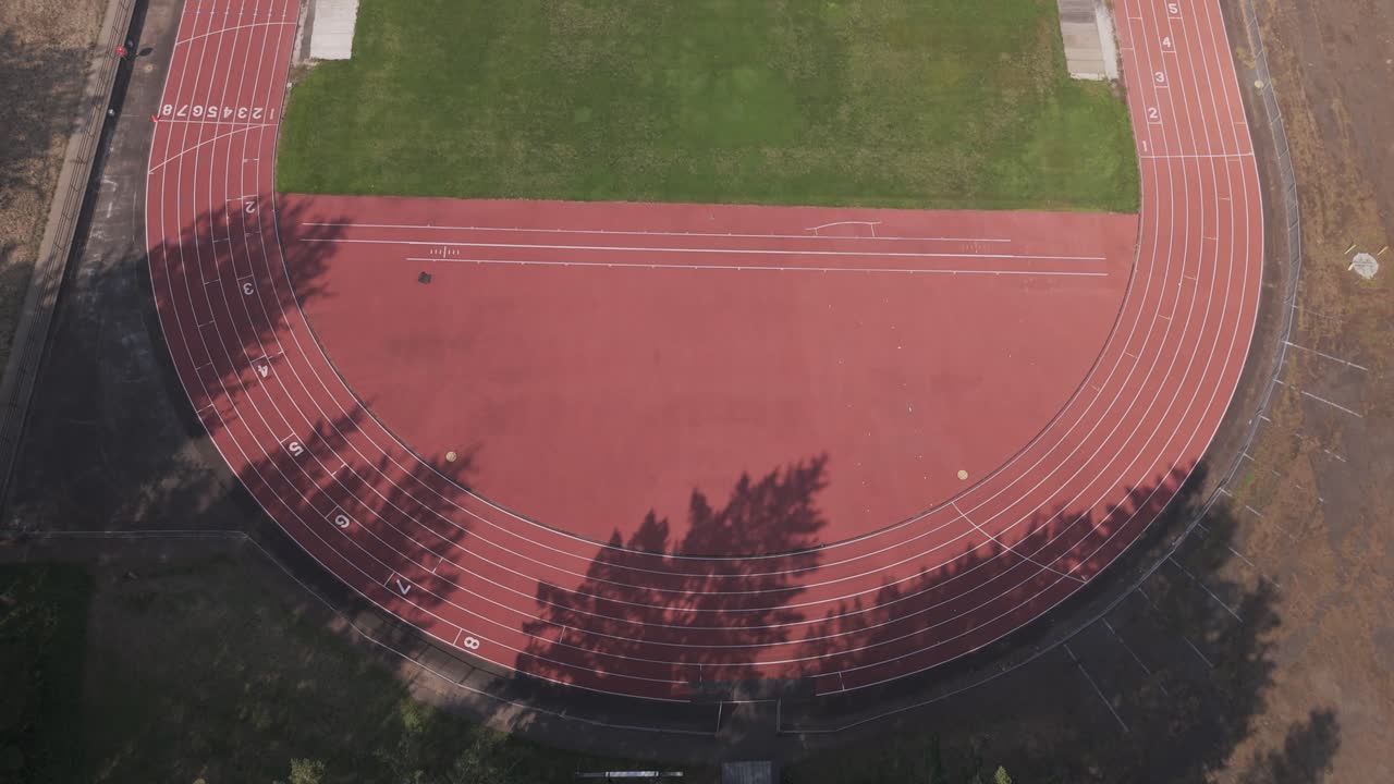 Aerial three quarter down angle tracking through the trees to reveal a college field and running track