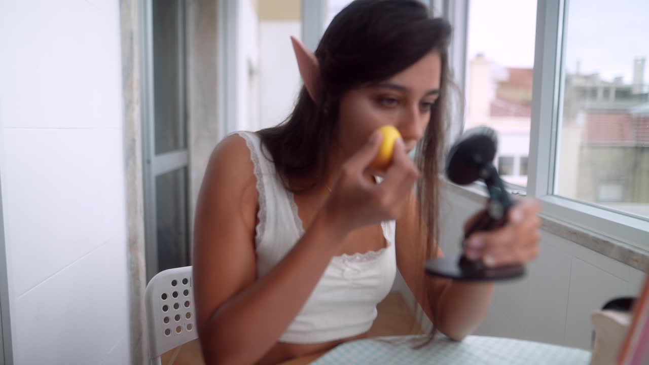 Young Woman with Elf Ears Applying Makeup with a Sponge