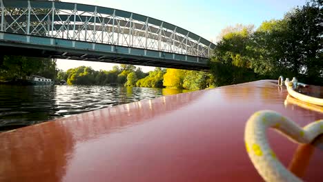 view towards the bow of a boat sailing on a river near a big iron bridge