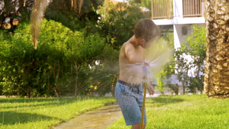 boy watering the lawn and getting wet