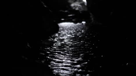 inside a cave in a mountain ocean brings water at a high tide. it’s dark. small ripples reflect light coming from entrance on the other end of a cave. it looks mysterious. cornwall cave. hd