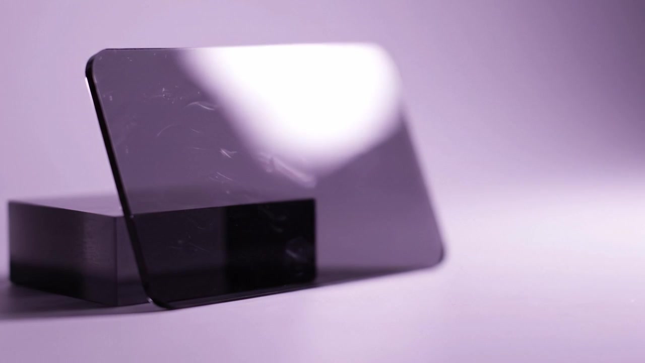 Expositor Contemporáneo con Superficie Reflectante que Muestra una Base Negra Elegante y una Capa Transparente, Capturado con Iluminación Púrpura Suave para un Atractivo Estético Moderno