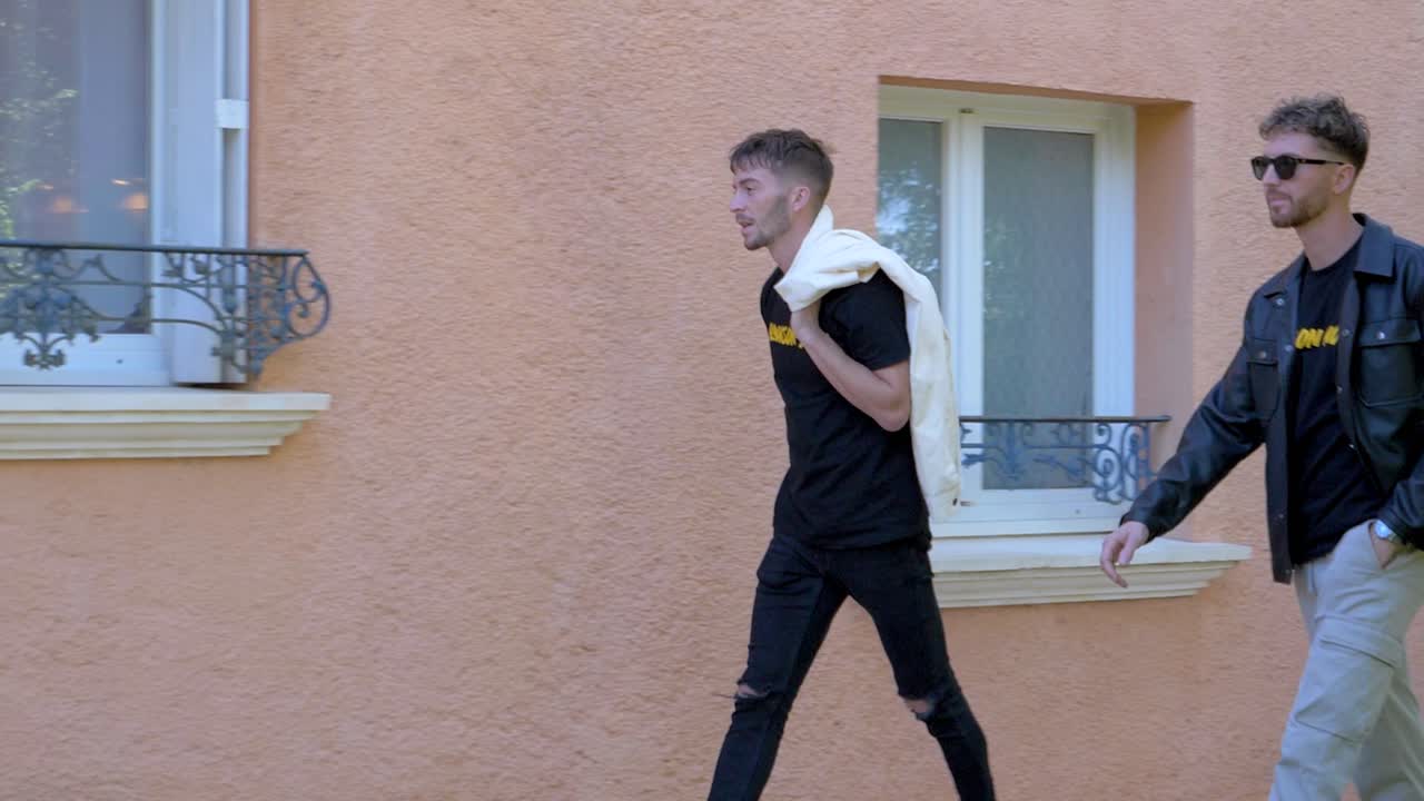 Slow motion shot of 2 young men walking along the street and entering a house