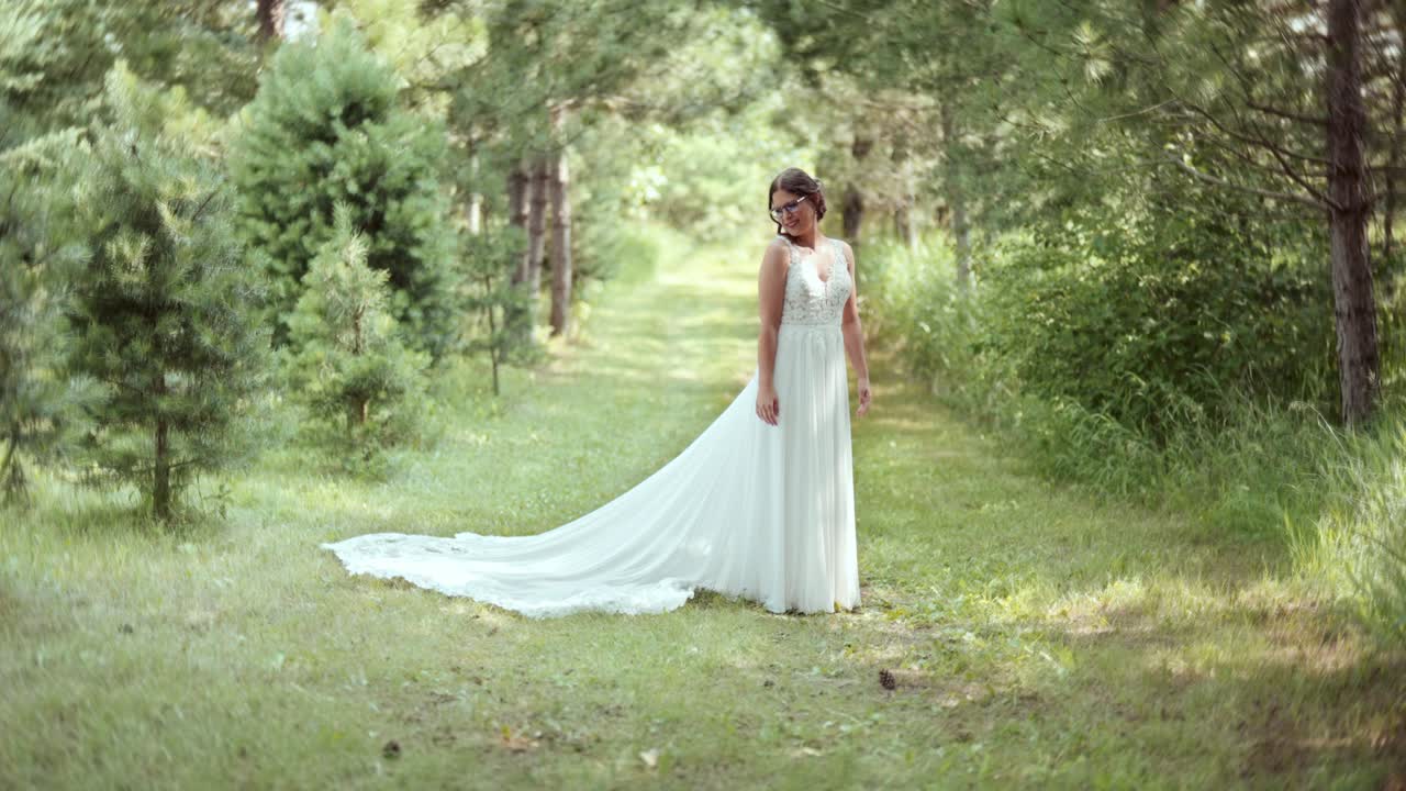 Slow-motion static shot of petite bride with glasses smiling at her dress train
