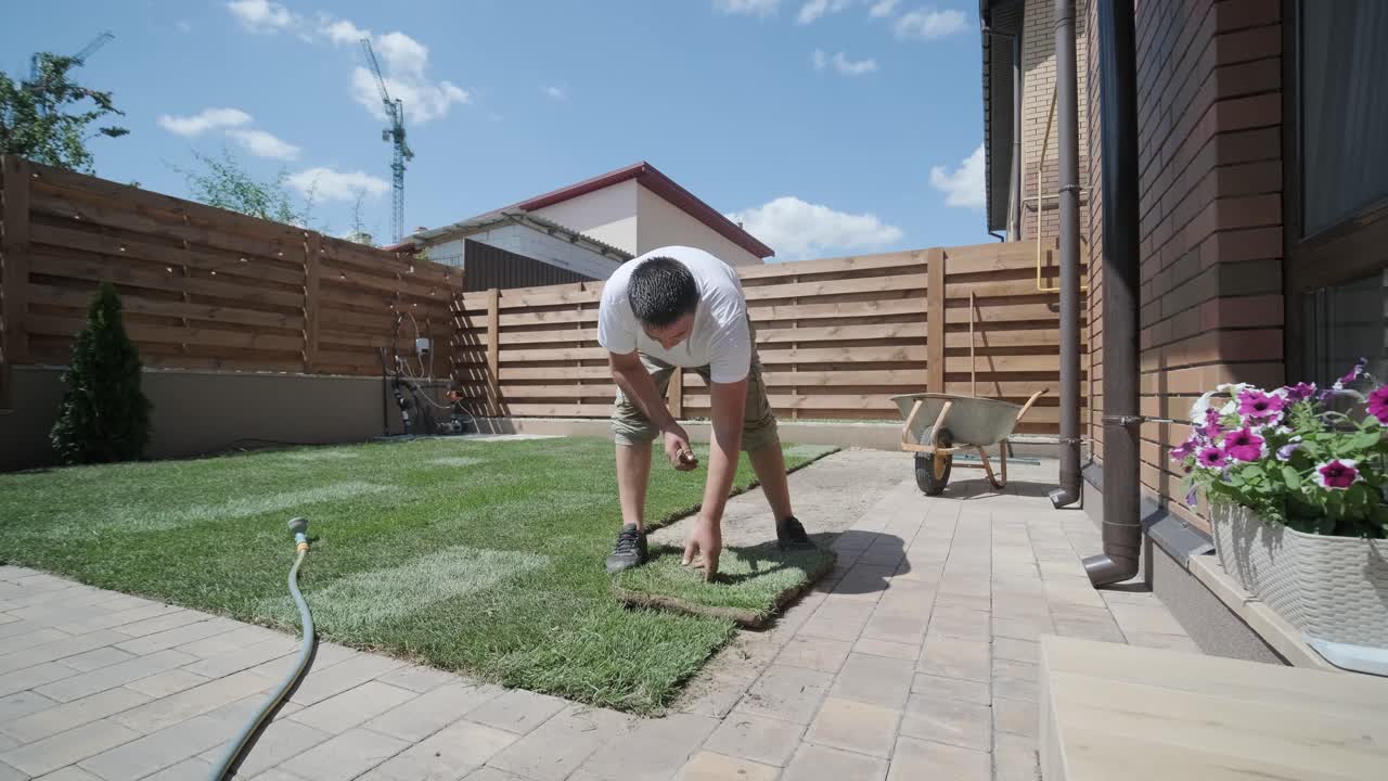 Man Laying Sod Grass in Backyard Garden for Lawn Installation and Landscaping Project, Focused on Home Improvement and Outdoor Maintenance for a Fresh, Green Lawn in a Residential Yard